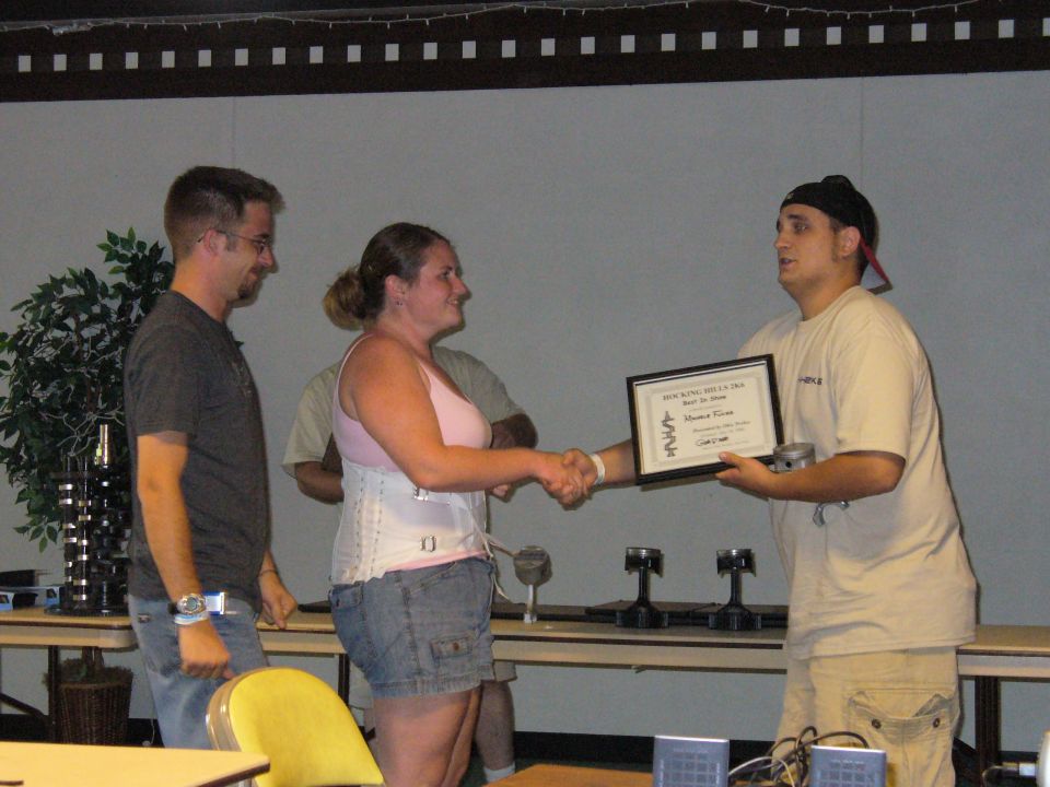Award ceremony with three people, one receiving a framed certificate and a metal part