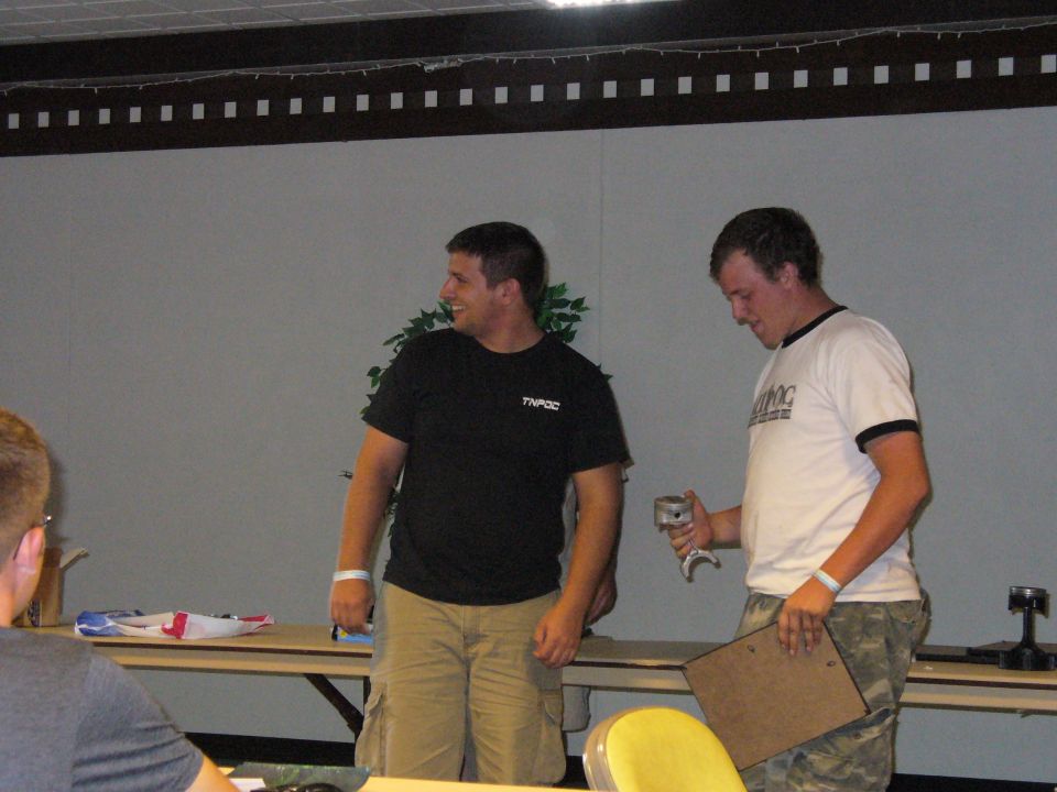 guy in black shirt and guy in white shirt stand near a table with items on it