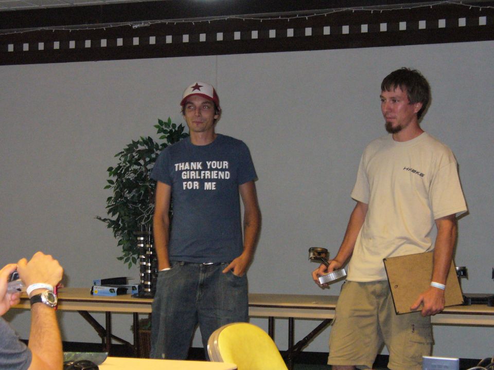 Two men stand in front of a screen; one wears a t-shirt that says "THANK YOUR GIRLFRIEND FOR ME"