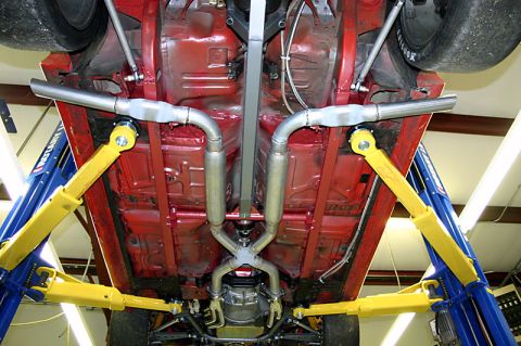 1993 Ford Mustang - The underside of a red vehicle is shown, a custom dual exhaust system and tires, lifted on a car hoist.