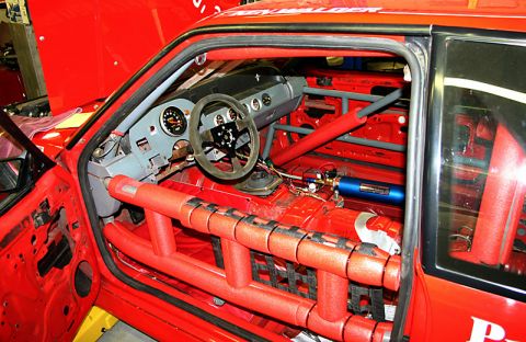 1993 Ford Mustang - Interior view of a stripped-down red race car, a roll cage, racing seat, and safety equipment.