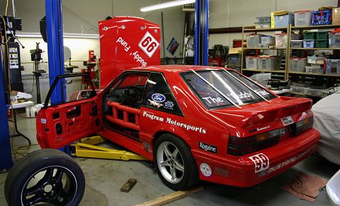 1993 Ford Mustang - Red 1993 Ford Mustang race car undergoing work in a garage with its doors open.