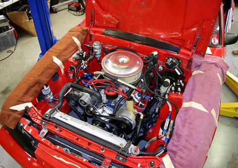 1993 Ford Mustang - The engine bay of a red car is shown with custom modifications and protective cloths covering parts of the fenders.