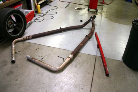 1993 Ford Mustang - Two rusty exhaust pipes and a tire are laid out on a concrete floor next to a red tool.
