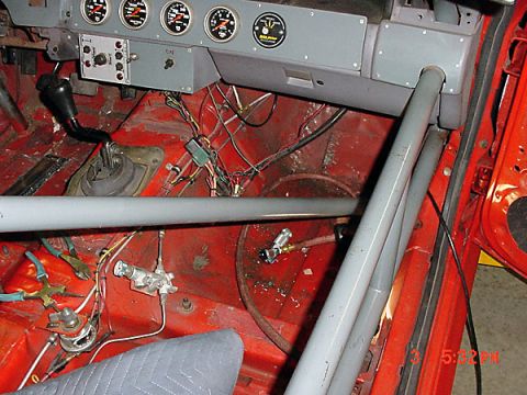 1993 Ford Mustang - The interior of a 1993 Ford Mustang shows a red floor, gray roll cage, dashboard gauges, and exposed wiring.