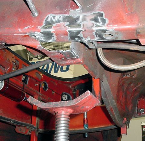 1993 Ford Mustang - Close-up view of the underbody of a red vehicle undergoing repairs, showing welded sections and a braided hose.
