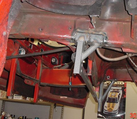 1993 Ford Mustang - Custom suspension components are welded onto the red car chassis, which is supported by jack stands.