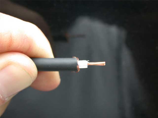 Hand holding a stripped coaxial cable end with copper braid and center conductor exposed