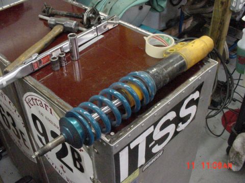 1993 Ford Mustang - A blue coilover shock absorber rests on a workbench next to tools and tape, suggesting a repair or rebuild process.