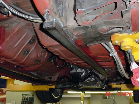1993 Ford Mustang - Underside view of a red vehicle, showing a custom reinforcement bar and transmission, possibly undergoing repairs or modifications.
