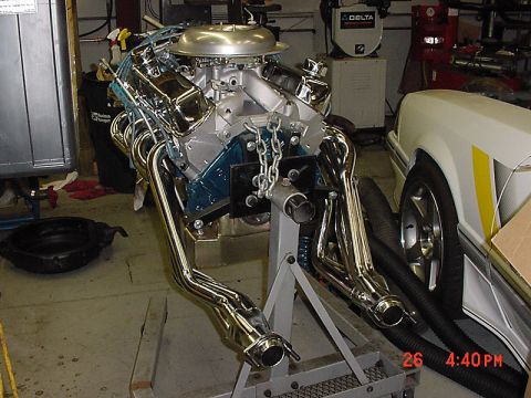 1993 Ford Mustang - A disassembled engine sits on a stand, with a portion of a white car visible to the right.