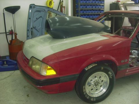 1990 Ford Mustang - A red 1990 Ford Mustang is shown with a large hood scoop and racing tires, indicating modifications for performance.