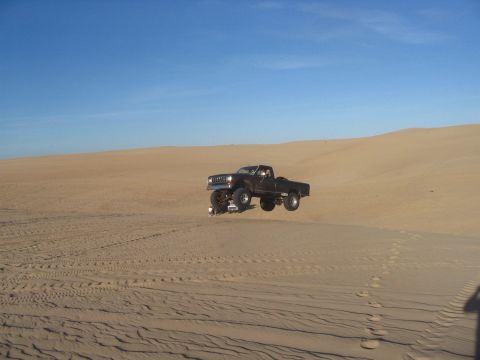 1985 Ford Ranger - A dark 1985 Ford Ranger is captured mid-air as it jumps over a sand dune.