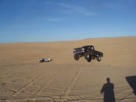 1985 Ford Ranger - Pickup truck catches air while driving over sand dunes with other vehicles present.