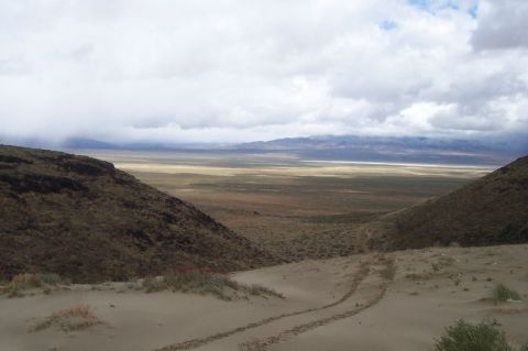 1994 Ford F-150 - Tire tracks mark a path through the sand, descending into a wide, desolate valley with distant mountains.