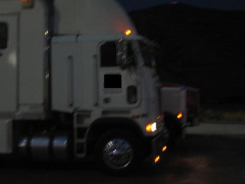 1990 Ford Bronco - white cabover semi tractor sits at night with amber marker and turn lights glowing, hills in the background.