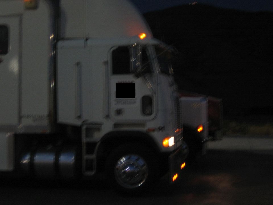Front of a white cabover semi truck at night with marker lights lit