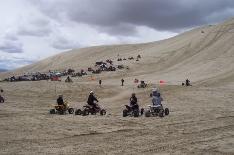 1994 Ford F-150 - A group of ATVs are seen riding on a large sand dune under a dramatic, cloudy sky.