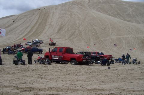 1994 Ford F-150 - A group of vehicles, including ATVs and trucks, gathered on a sandy dune landscape under a cloudy sky.