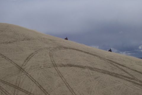 1994 Ford F-150 - Two ATVs navigate a sandy incline, leaving tracks on the dune under a dramatic sky.