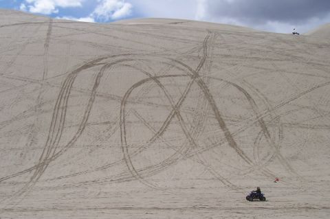 1994 Ford F-150 - ATVs leave tracks on a vast sand dune under a cloudy sky.