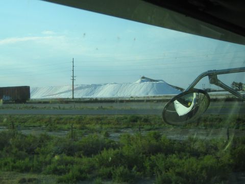 1990 Ford Bronco - Seen through a vehicle window with a side mirror, large white mounds and a rail car sit across a scrubby field.