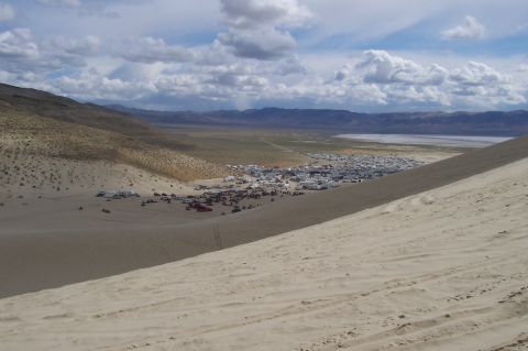 1994 Ford F-150 - A wide view of a desert landscape a distant encampment and numerous vehicles scattered across the terrain under a cloudy sky.