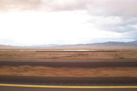 1994 Ford F-150 - A wide desert landscape stretches out with a road in the foreground and mountains in the distance under a cloudy sky.