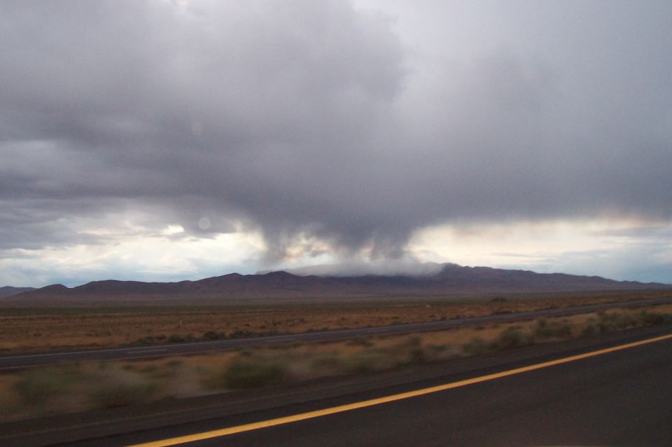 Storm clouds gathering over a mountain range with a highway in the foreground