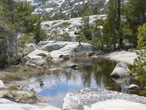 1986 Ford Bronco - A mountain scene a tranquil pond reflecting the sky amidst large granite boulders and evergreen trees.