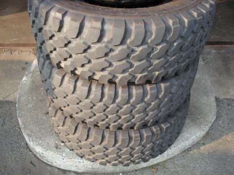 1994 Ford Bronco - Three off-road tires are stacked on a concrete surface, showing their aggressive tread patterns.
