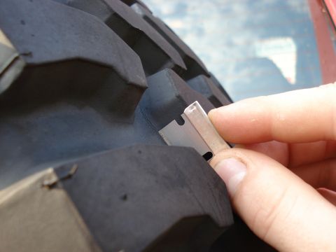 1994 Ford Bronco - Measuring tire tread depth with a razor blade against a large off-road tire.