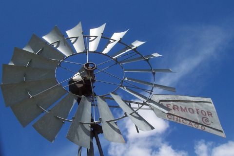 1994 Ford F-150 - A windmill with metal blades stands against a bright blue sky with scattered clouds.