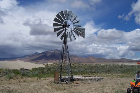 1994 Ford F-150 - A windmill stands tall against a dramatic sky in a desert landscape, with mountains in the distance and an ATV parked nearby.