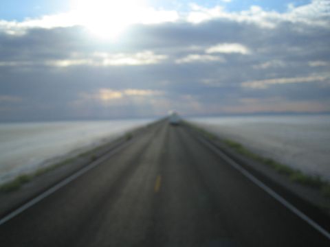 1990 Ford Bronco - two-lane road stretches into the hazy distance across flat terrain under sun rays breaking through clouds.