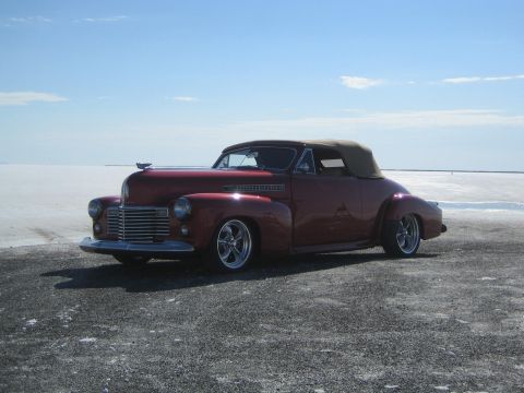 1990 Ford Bronco - maroon custom 1940s-style convertible street rod with a tan soft top sits on a white salt flat under blue sky.