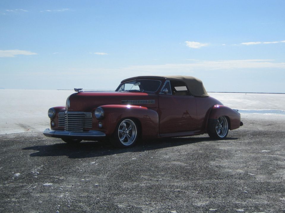 maroon custom convertible street rod with tan top parked on a salt flat