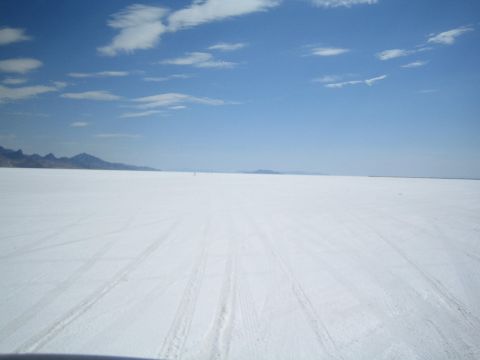 1990 Ford Bronco - vast flat white salt expanse with faint tire tracks stretches to distant mountains under a blue sky with wispy clouds.
