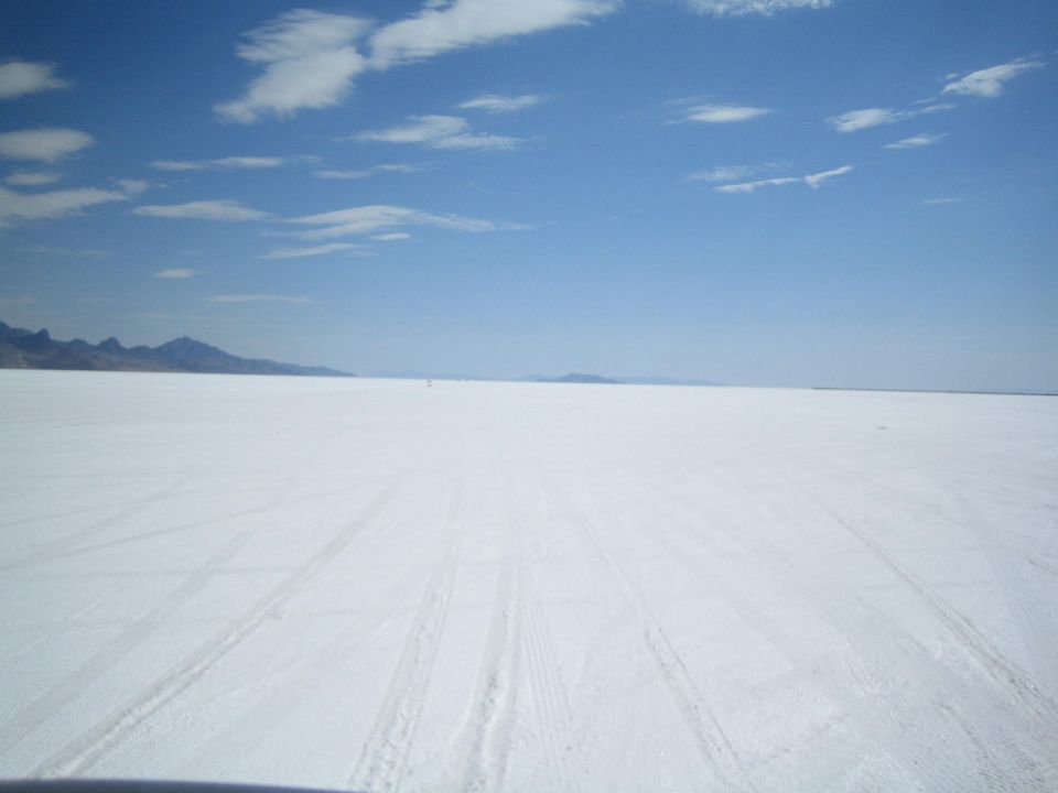 vast white salt flat with tire tracks and distant mountains under blue sky