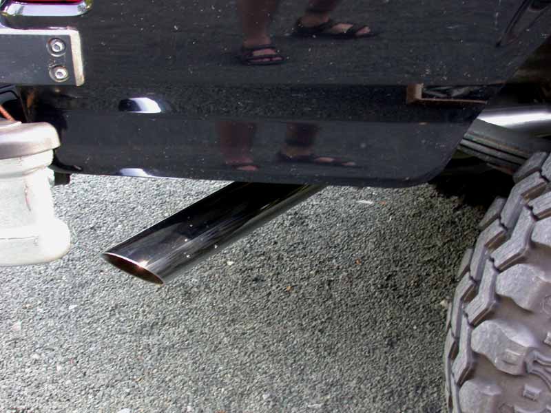 Chrome angle-cut exhaust tip under the rear of a black truck on gravel
