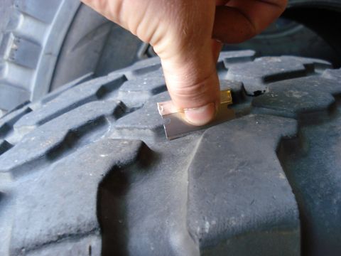 1994 Ford Bronco - A hand checks the tread depth of a large off-road tire with a razor blade.