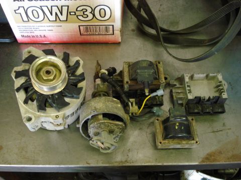 1994 Ford Bronco - Various automotive ignition system components and an alternator are laid out on a metal surface.