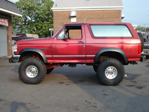 1994 Ford Bronco - Driver-side profile of a red lifted Ford Bronco full-size SUV with removable hardtop, black fender flares and BRONCO body-side badging, sit…