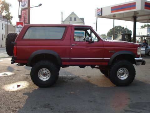 1994 Ford Bronco - Driver-side profile of a red lifted Ford Bronco with removable hardtop, black fender flares, tow mirrors and a swing-away rear tire carrier…