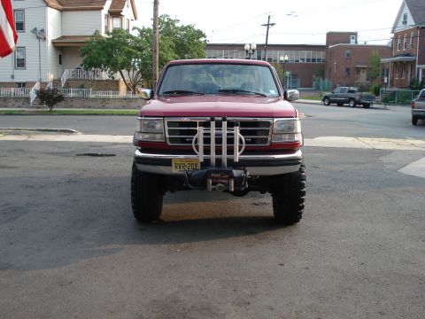 1994 Ford Bronco - Head-on front view of a red lifted full-size Ford Bronco parked on a residential street, showing the chrome grille and bumper, dual rectang…