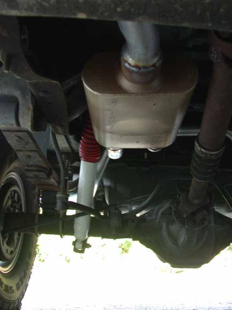 1996 Ford Bronco - Underbody view of a freshly installed oval performance muffler with a raw welded inlet pipe, mounted near the rear axle. A white shock abso…