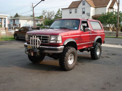 1994 Ford Bronco - Red lifted Ford Bronco with removable hardtop parked on a street corner lot in a residential neighborhood, seen from the front three-quarte…