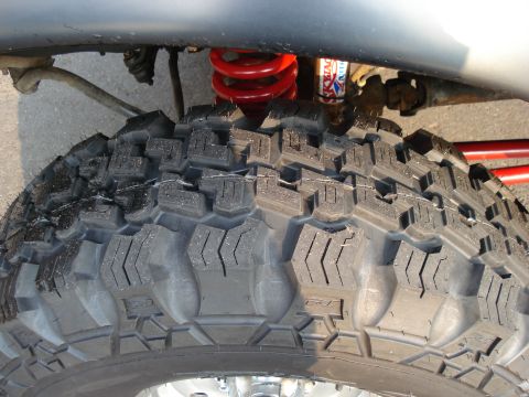 1994 Ford Bronco - Overhead close-up looking down into a front wheel well, showing the aggressive blocky tread of a nearly new mud-terrain tire. Behind it are…