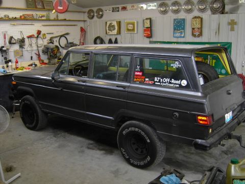 1977 Jeep Wagoneer - A 1977 Jeep Wagoneer is parked inside a garage, surrounded by tools and automotive memorabilia.