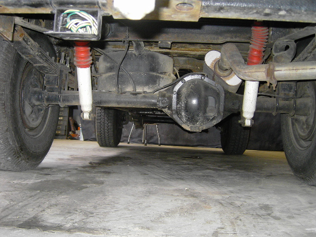Underbody view of a solid rear axle with leaf springs, drum brakes and new white shocks with red boots